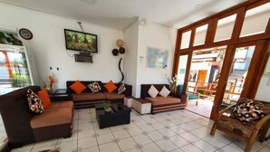 A living room with a sofa set, a coffee table, and a wooden chair. There is a television mounted on the wall and a window with a view of the outside. - Hotel Deja Vu (Puerto Ayora)