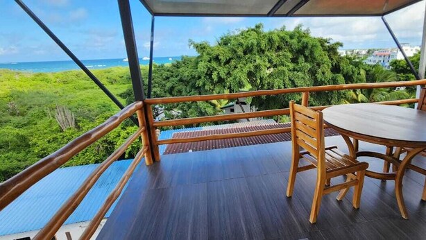 A wooden deck with a table and chairs, overlooking a lush green landscape and the ocean. - Hotel Deja Vu (Puerto Ayora)