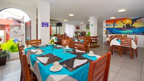 A dining area with tables set for four, wooden chairs, and a large mural on the wall. - Hotel Deja Vu (Puerto Ayora)