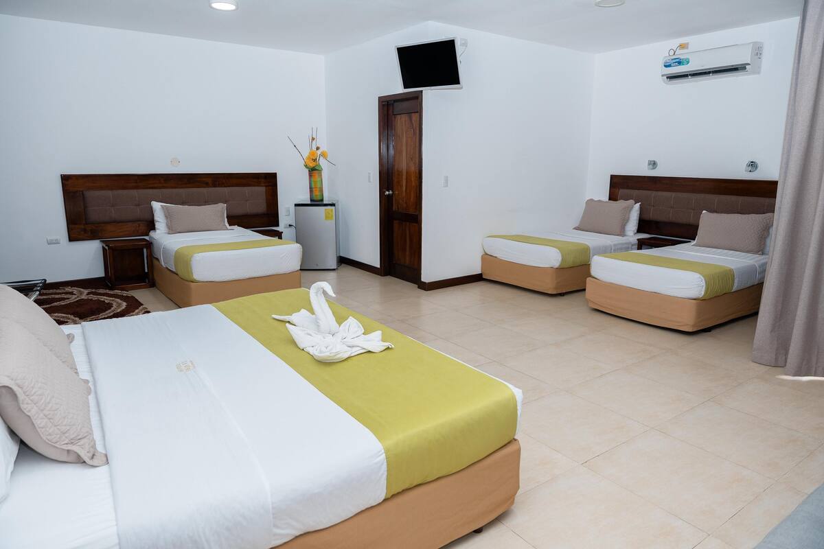 Une chambre d’hôtel avec deux lits simples, un lit double, un petit réfrigérateur, une télévision et un appareil de climatisation.