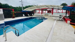 A swimming pool with a glass enclosure, surrounded by lounge chairs and a covered seating area. - Hotel Deja Vu (Puerto Ayora)