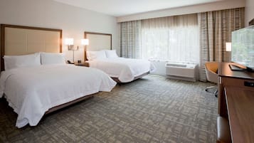 A hotel room with two beds, a desk, a chair, a TV, and an air conditioning unit.