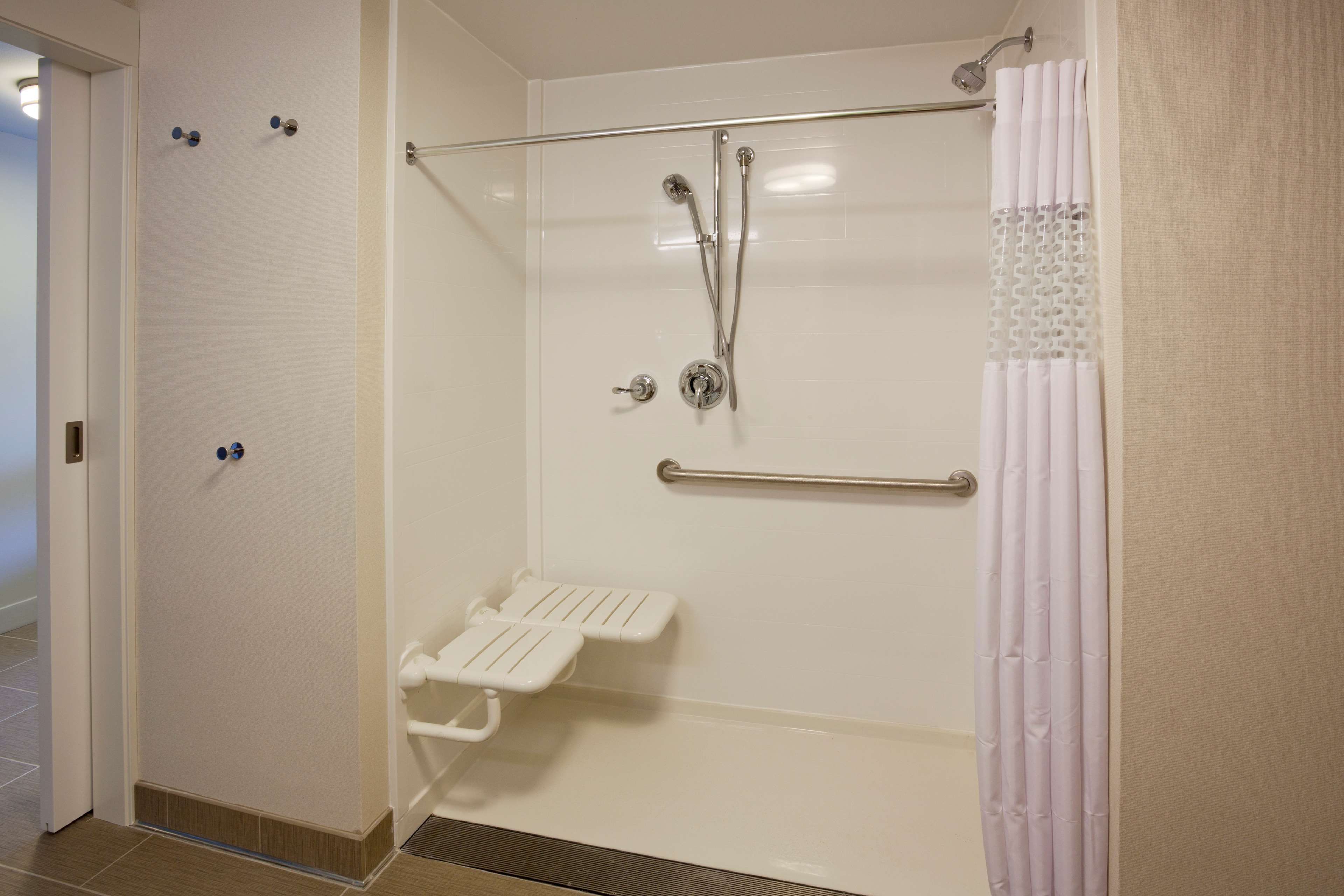 A walk-in shower with a glass door, a white shower seat, and a grab bar.