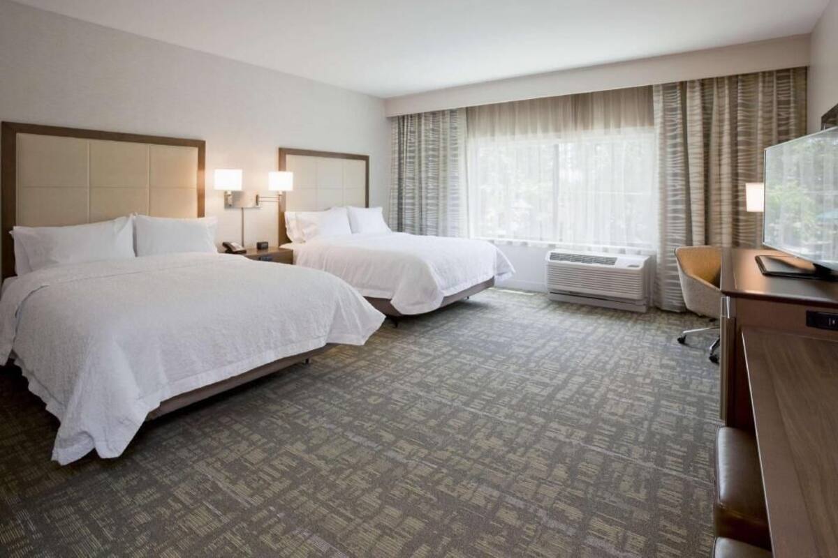 A hotel room with two beds, a desk, a TV, and a window with curtains.