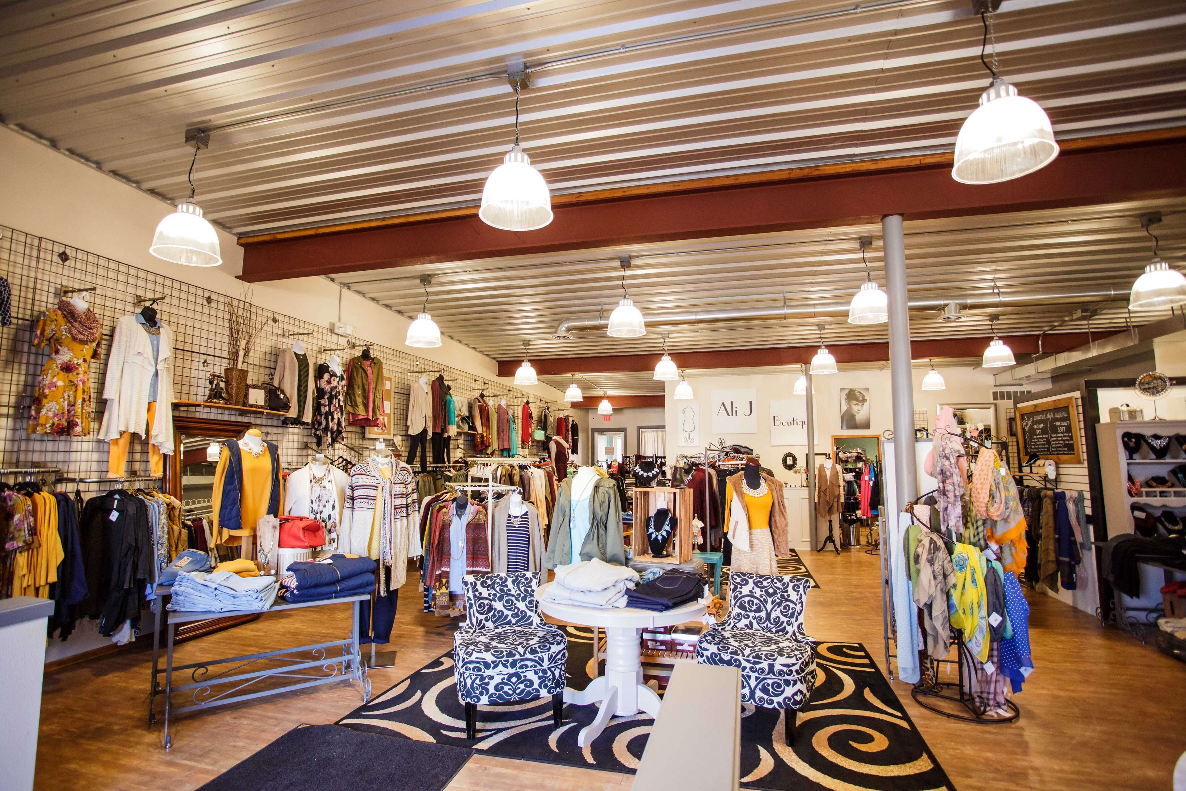 A clothing store with racks of clothes, a seating area with patterned chairs, and hanging lights on the ceiling.