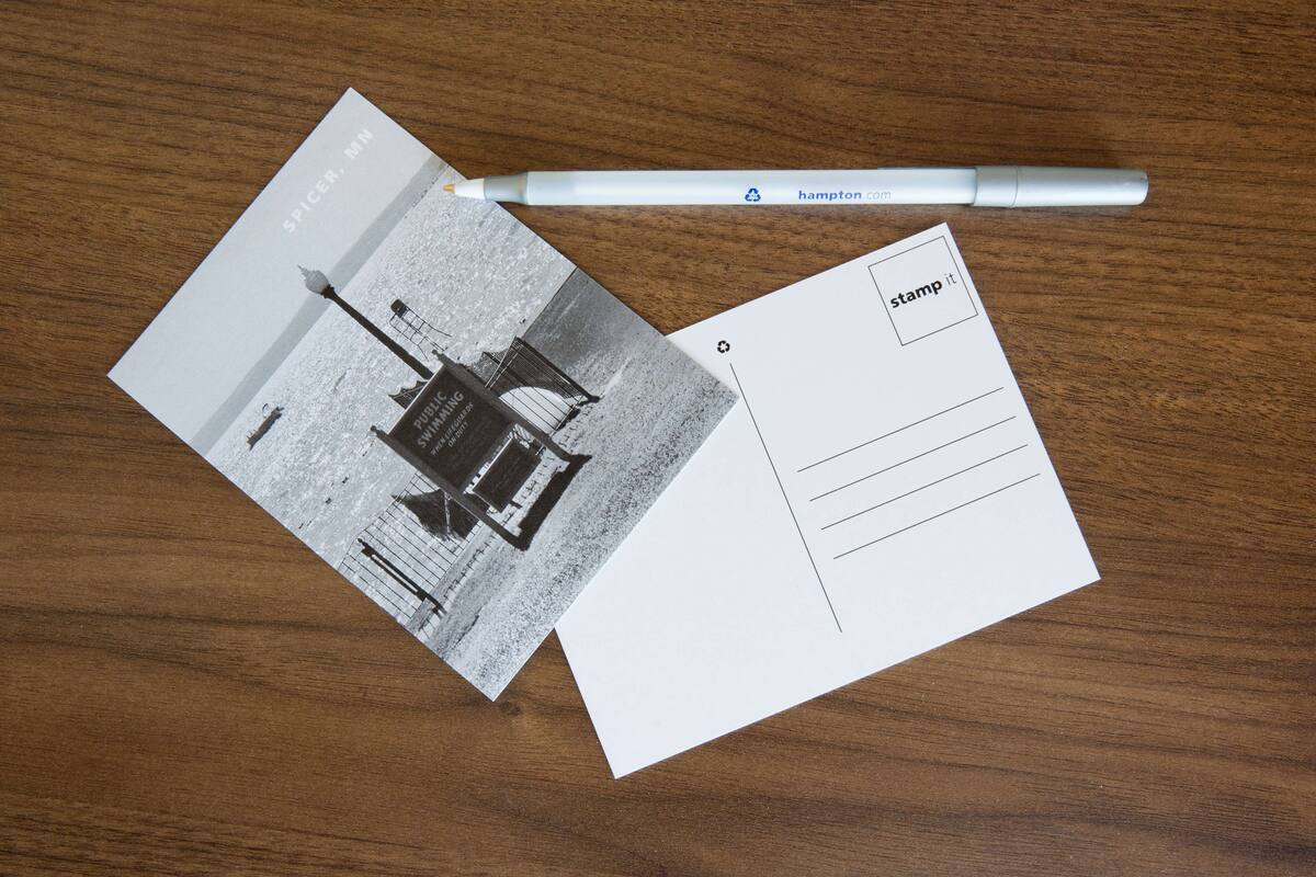 A postcard with a lighthouse image, a pen, and a blank postcard with "stamp it" text.