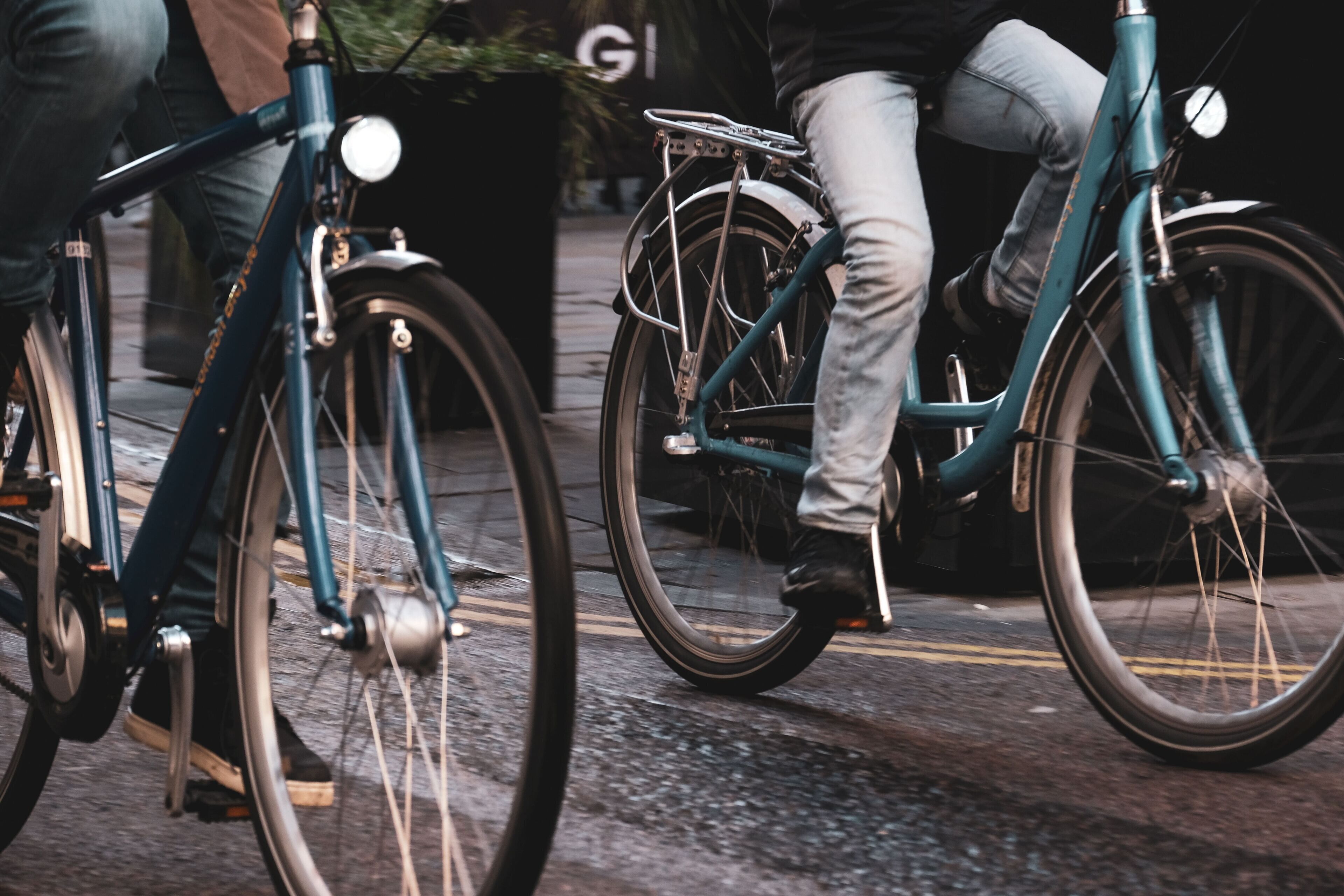 A close-up of a teal bicycle with a front light and a rear rack, parked on a paved surface.