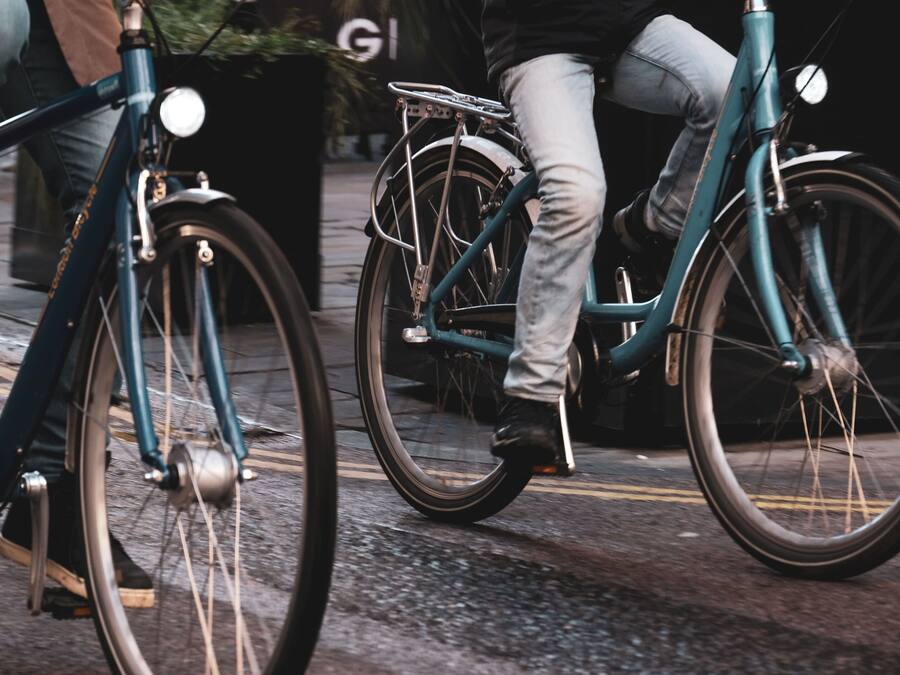 A close-up of a teal bicycle with a front light and a rear rack, parked on a paved surface.