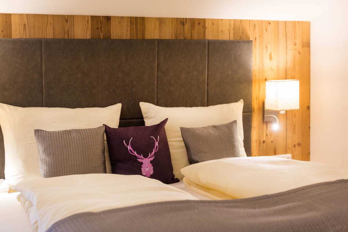 A bed with multiple pillows, a headboard, and a wall-mounted lamp.