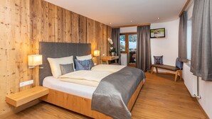 Un dormitorio moderno con una pared de madera, una cama grande con cabecera, lámparas de noche, un banco y vistas al exterior.