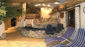Un espacio exterior acogedor con una chimenea de piedra, sillones de descanso y una escalera de madera que lleva a un nivel superior.