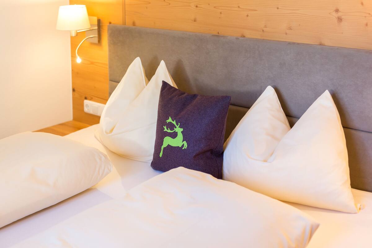 A bed with white pillows and a single purple pillow with a deer design.
