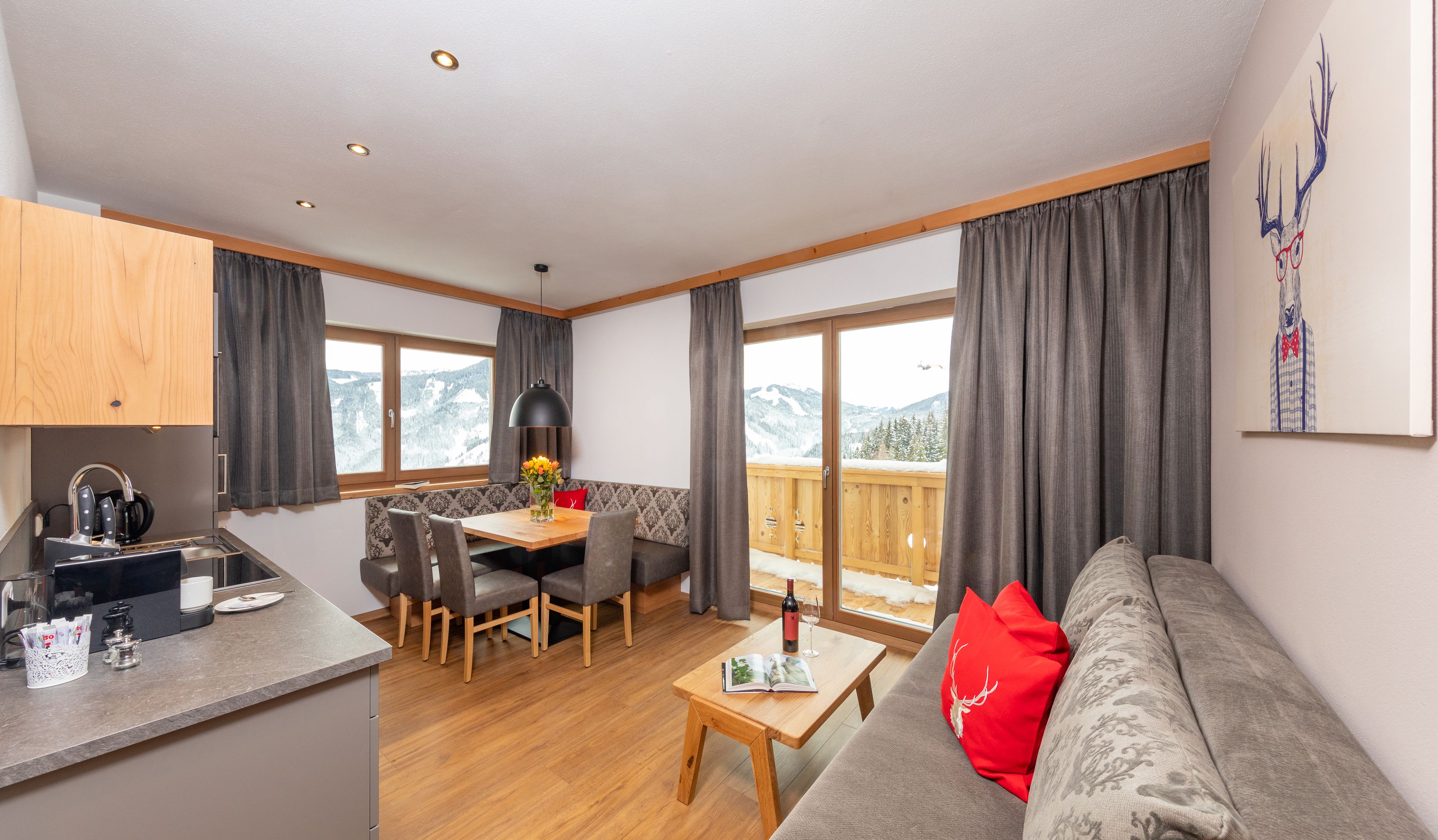 A modern living room with a wooden dining table, grey sofa, and a balcony with a mountain view.