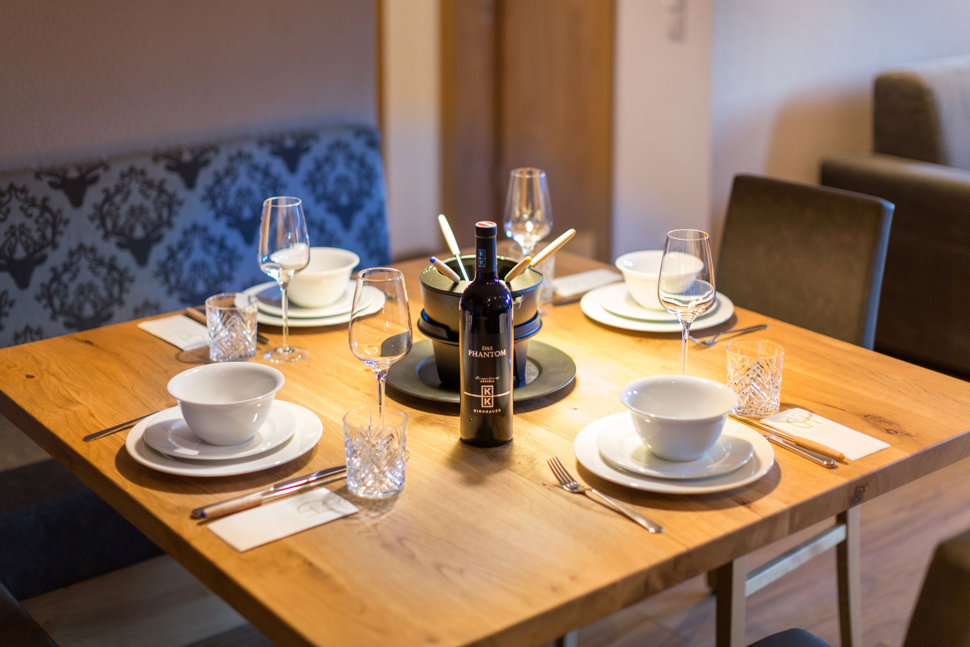 A dining table set with white bowls, plates, and cutlery, a bottle of wine, and glasses.