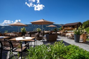 An outdoor patio with tables and chairs, umbrellas, and potted plants. - Das Grünholz Aparthotel (Muehlbach Am Hochkoenig)