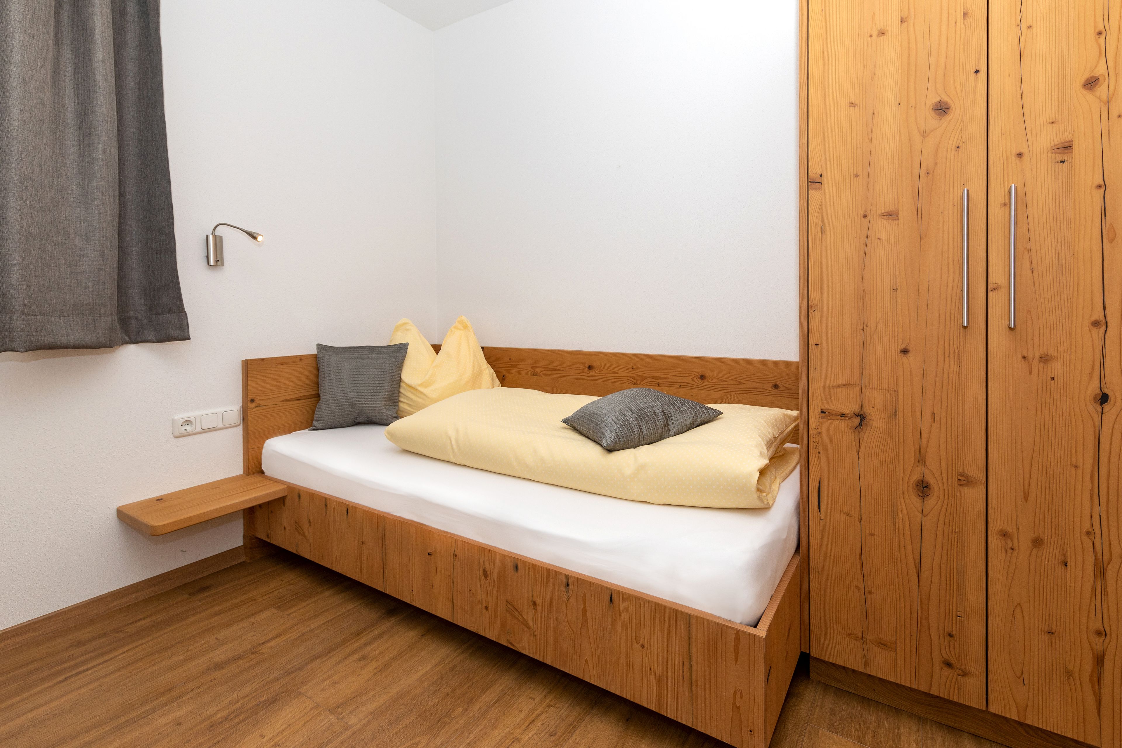 A single bed with a wooden frame, a bedside table, and a wardrobe with two doors.