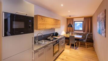 A compact kitchen with a microwave, oven, and sink. There's a dining area with a table and chairs, and a window with a view of a snowy landscape.