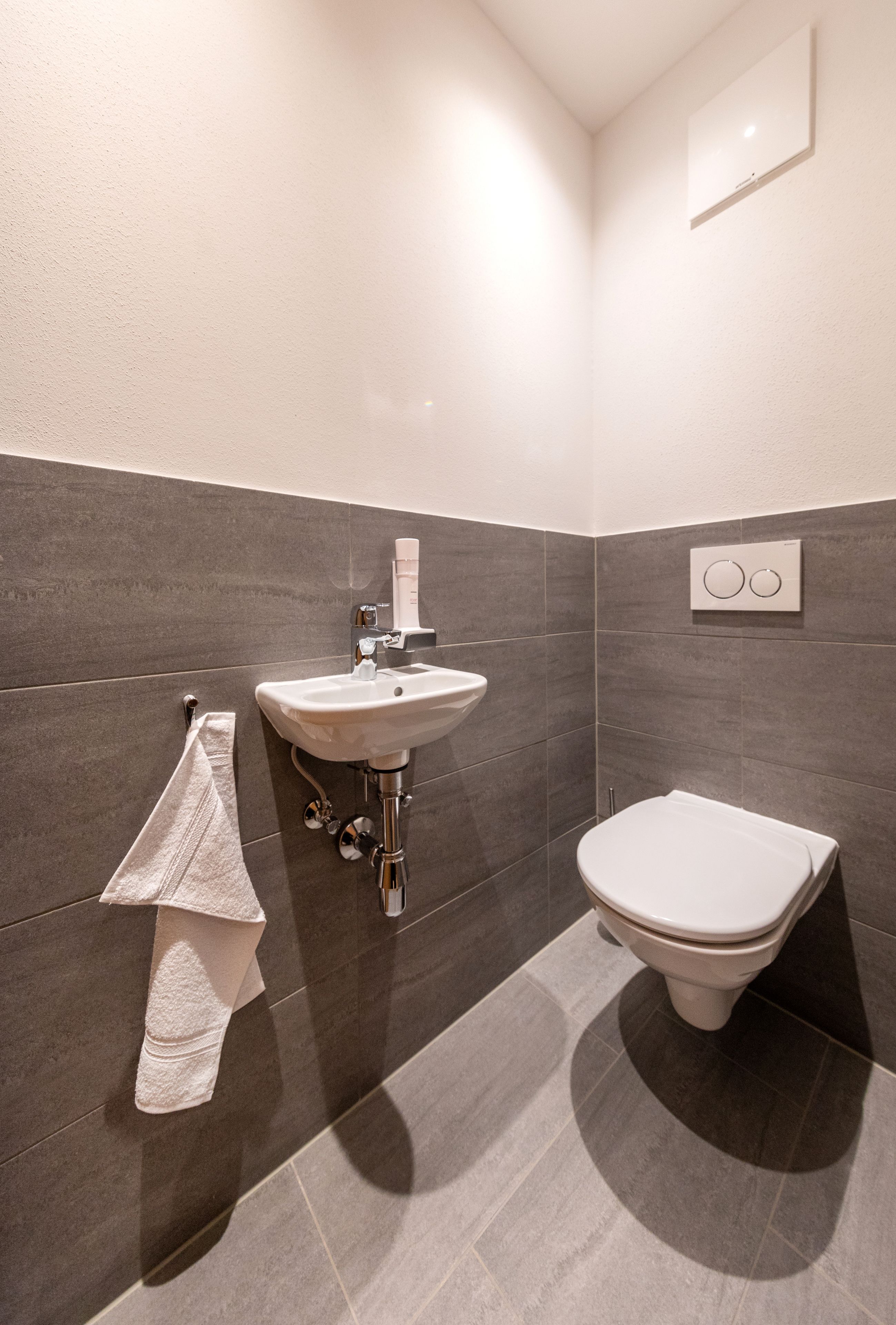 Un baño moderno con lavabo blanco, inodoro y toalla colgada en la pared.