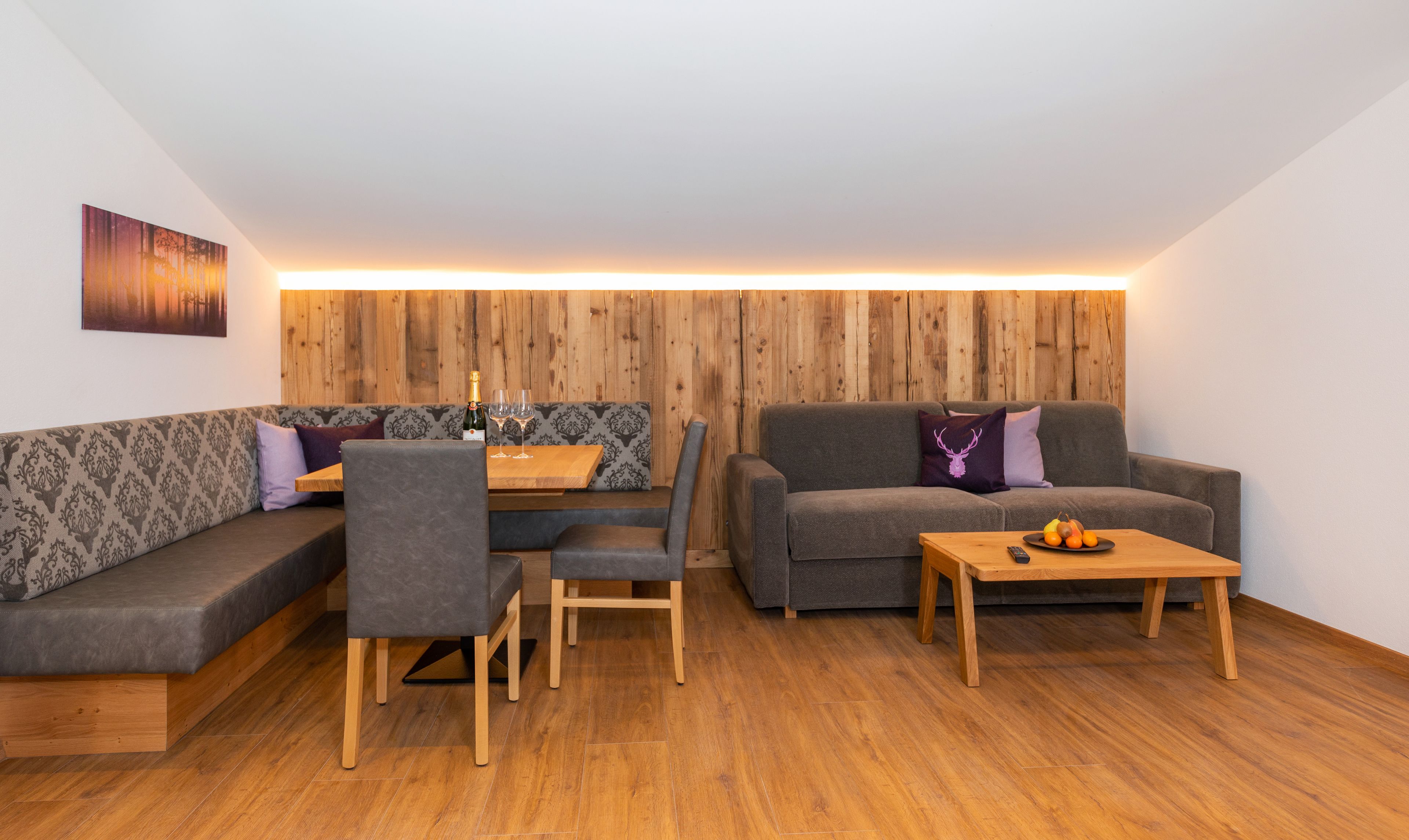 Un salon moderne avec un plancher en bois, des canapés gris, une table basse en bois et un luminaire fixé au mur.