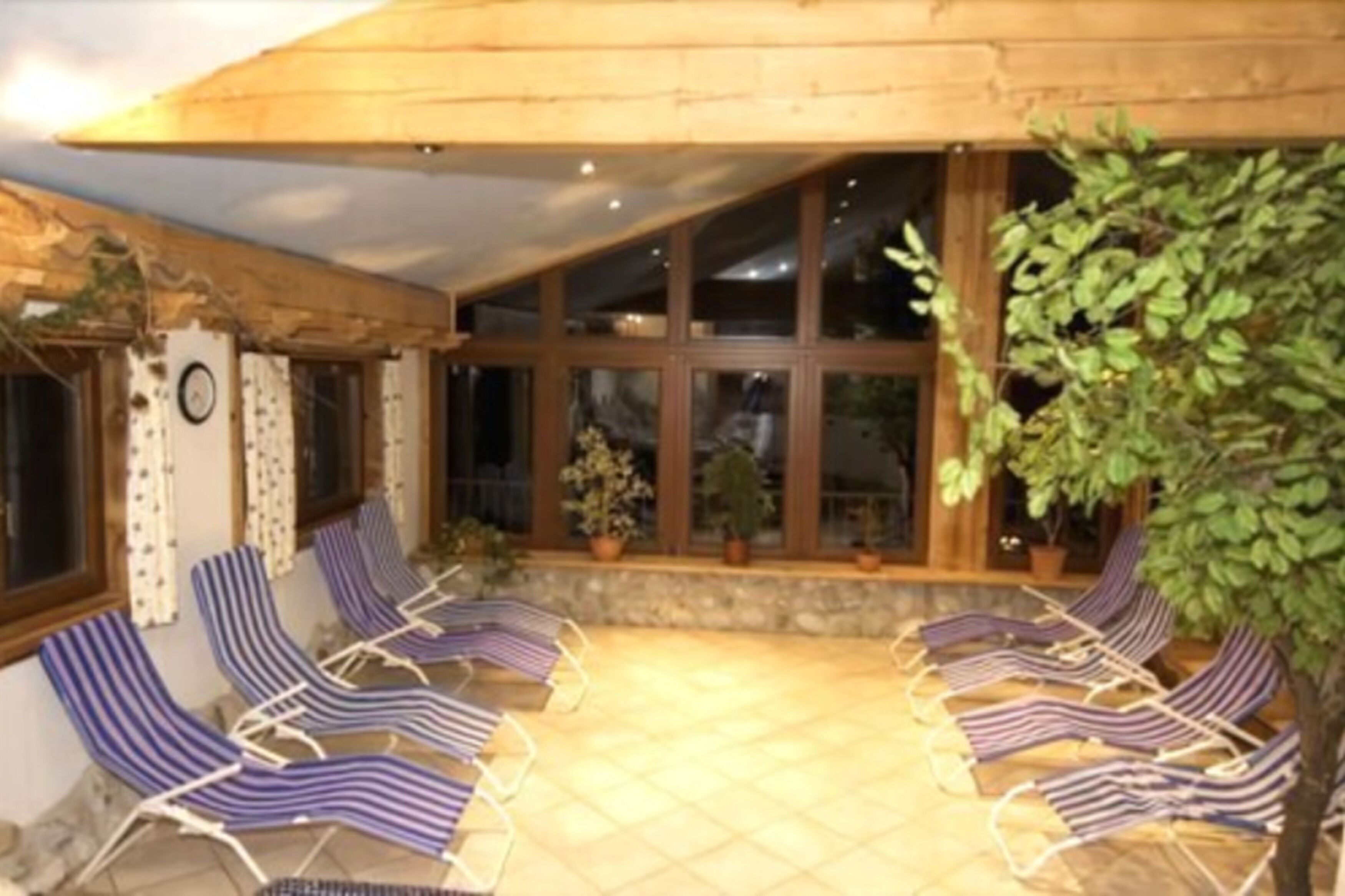 A covered outdoor seating area with striped lounge chairs and potted plants.