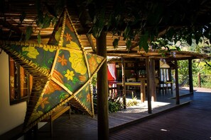 Une terrasse en bois dotée d’un espace salon couvert, d’un élément décoratif suspendu et offrant une vue sur la végétation environnante.