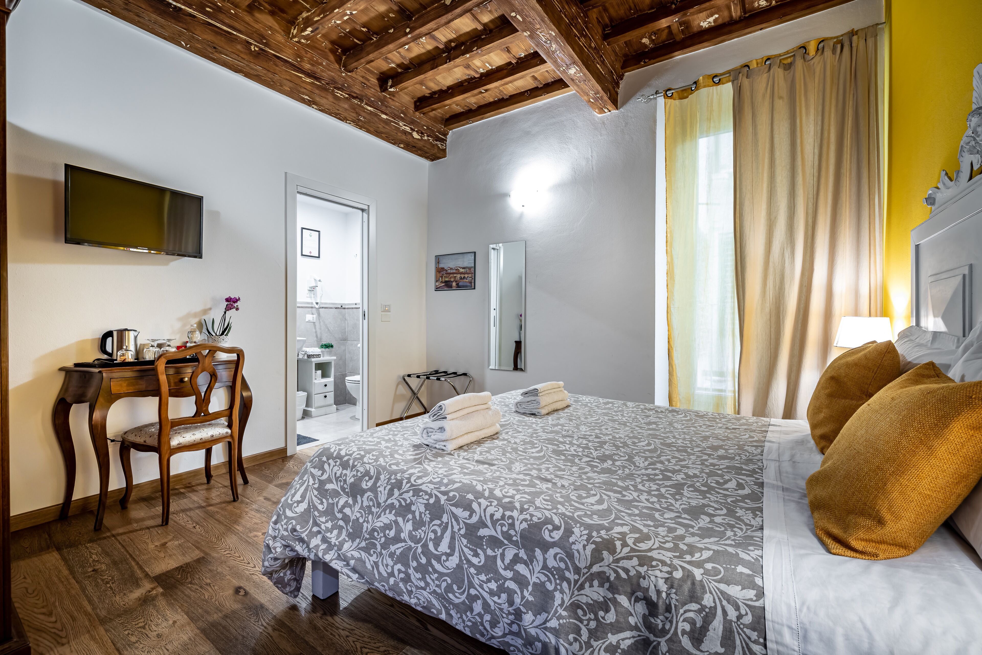 A bedroom with a bed, wooden desk, chair, and a television on the wall.
