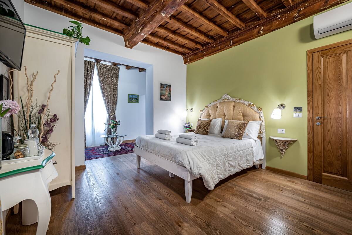 A bedroom with a wooden ceiling, a bed with white bedding, a bedside table with a lamp, and a green wall.
