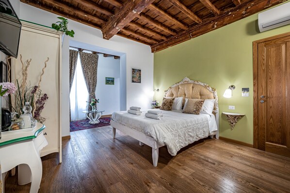Un dormitorio con techo de madera, cama con ropa blanca, mesita de noche con lámpara y pared verde.