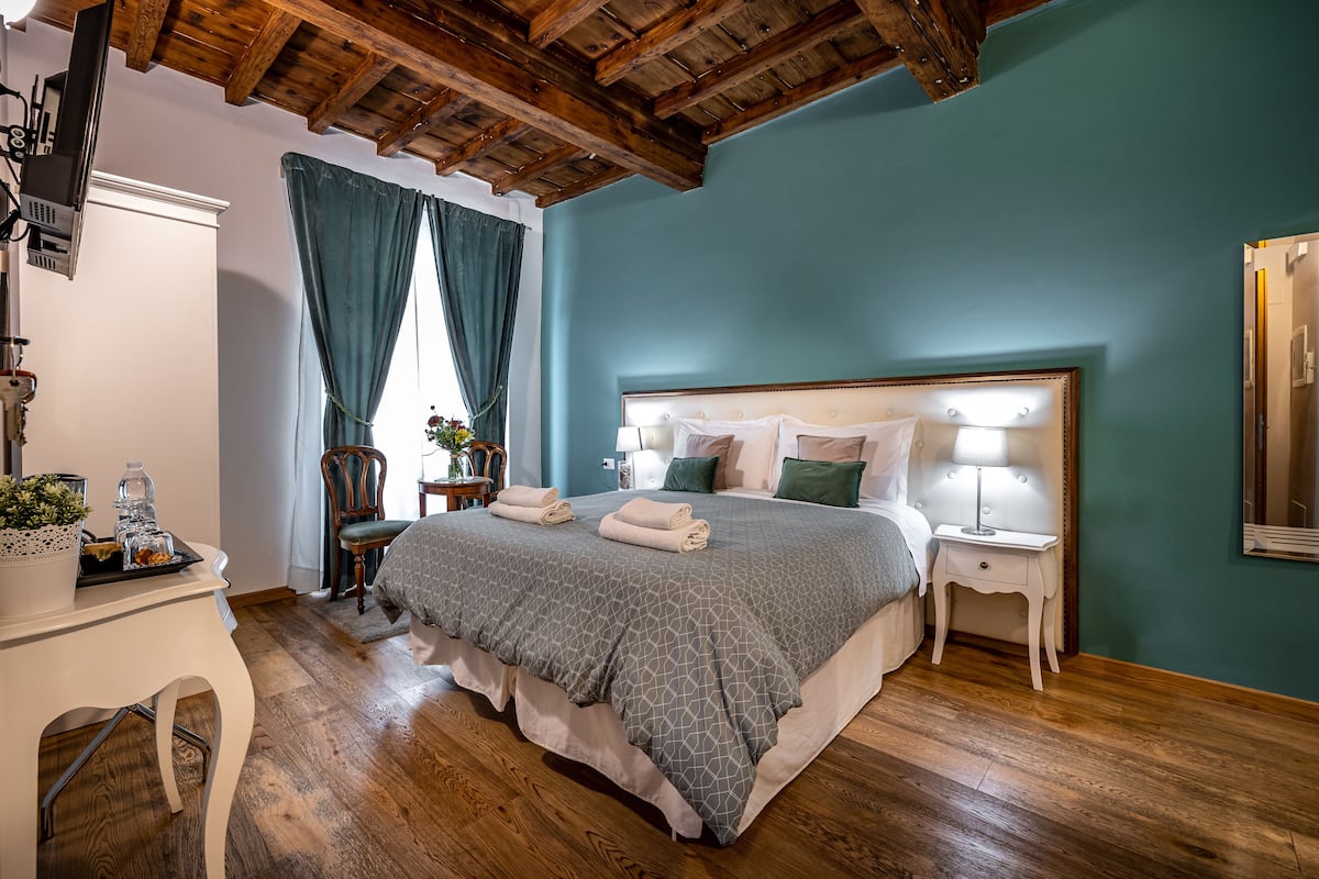 A bedroom with a large bed, wooden floor, and a ceiling with exposed beams.