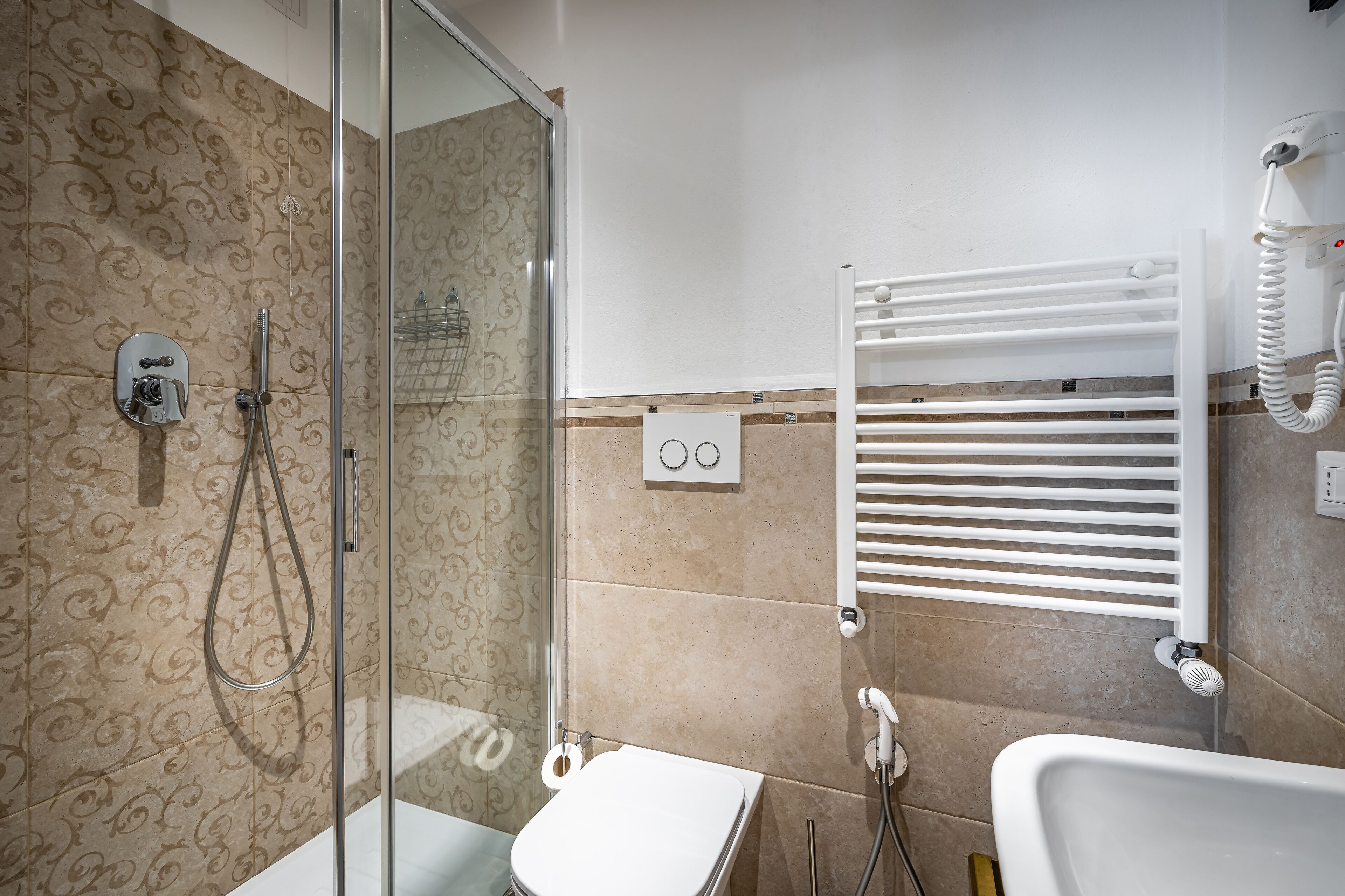 Een badkamer met een glazen douchecabine, een wit toilet, een witte wastafel en een handdoekrek.