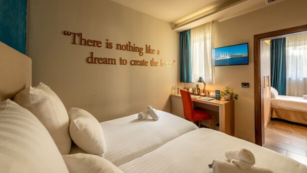 Ein Hotelzimmer mit einem großen Bett, einem Schreibtisch und einem an der Wand befestigten Fernseher.