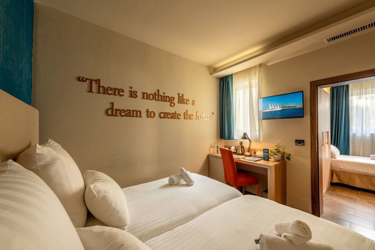 A hotel room with a large bed, a desk, and a television on the wall.