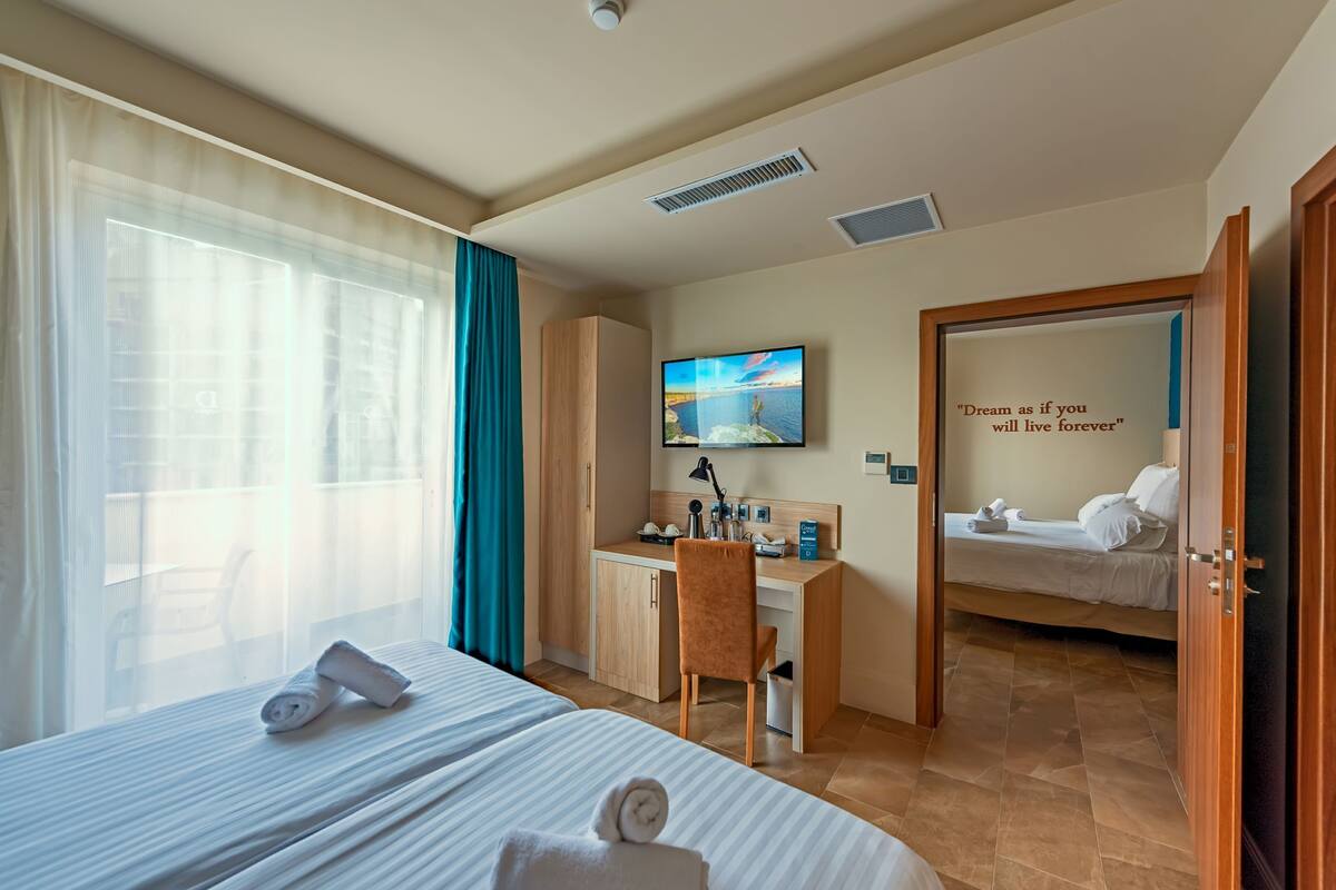 A hotel room with two beds, a desk, a TV, and a motivational quote on the wall.