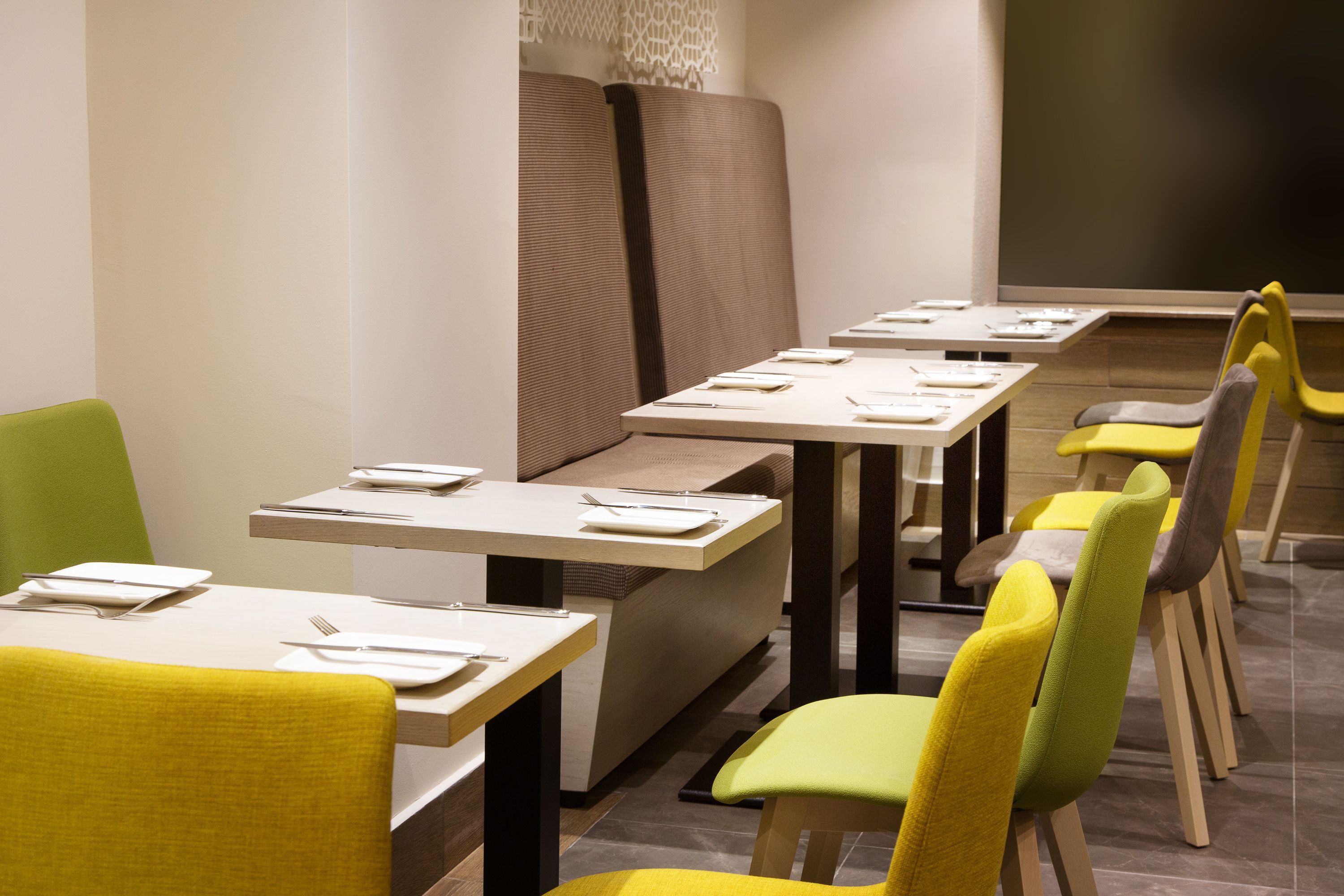 A modern dining area with multiple tables and chairs, each set with white plates and cutlery.