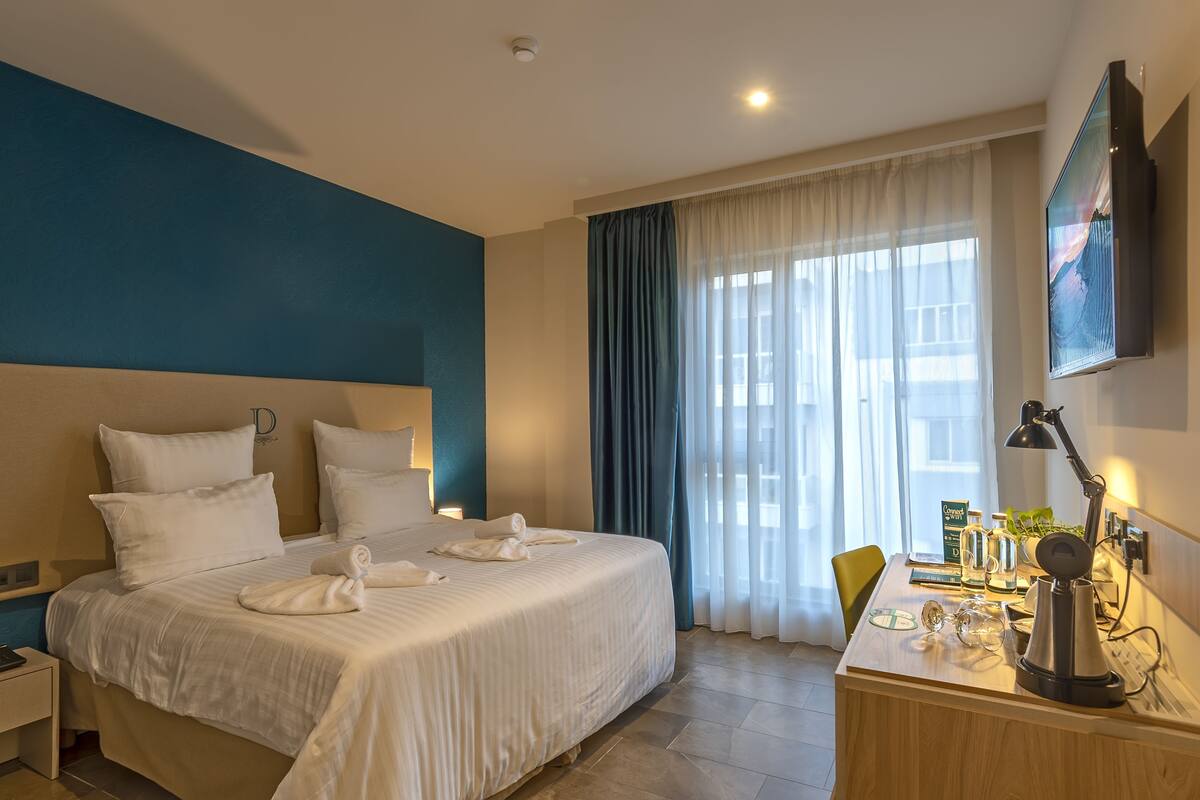 A hotel room with a bed, a desk, a chair, a TV, and a window with curtains.