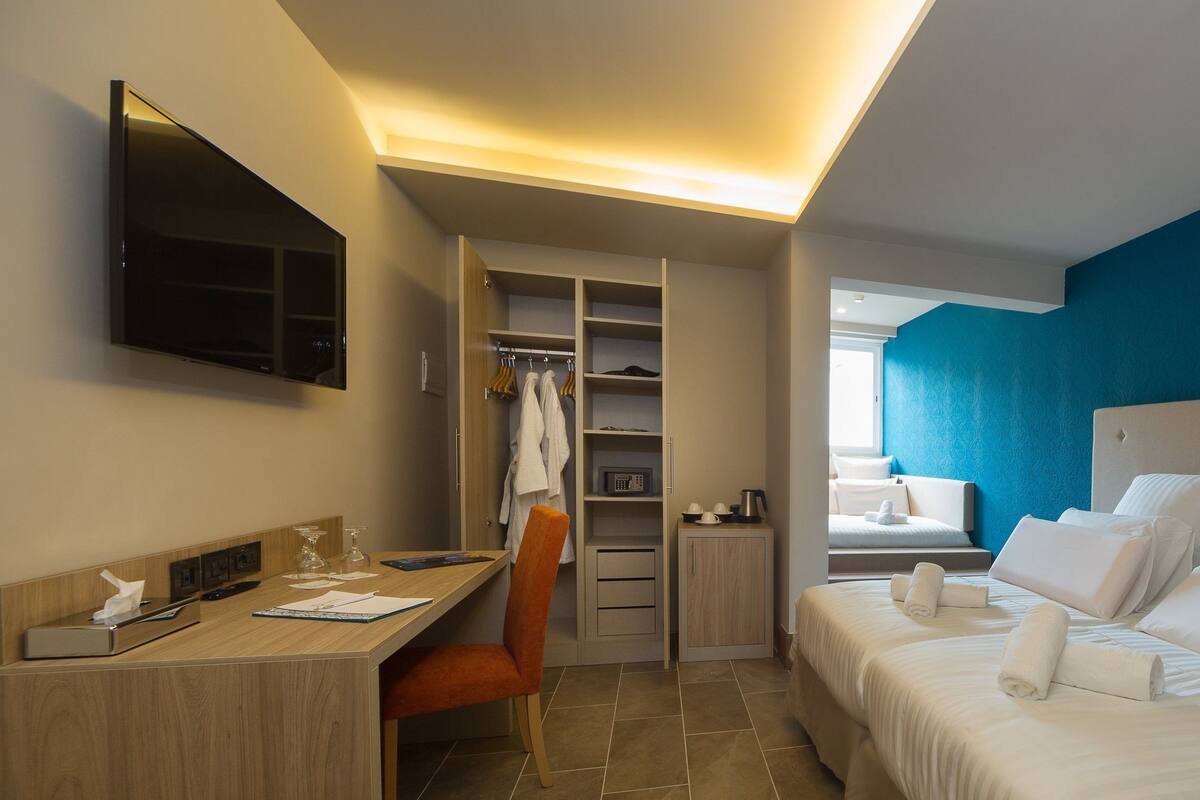 A hotel room with a bed, a desk, a chair, a wardrobe, and a television.