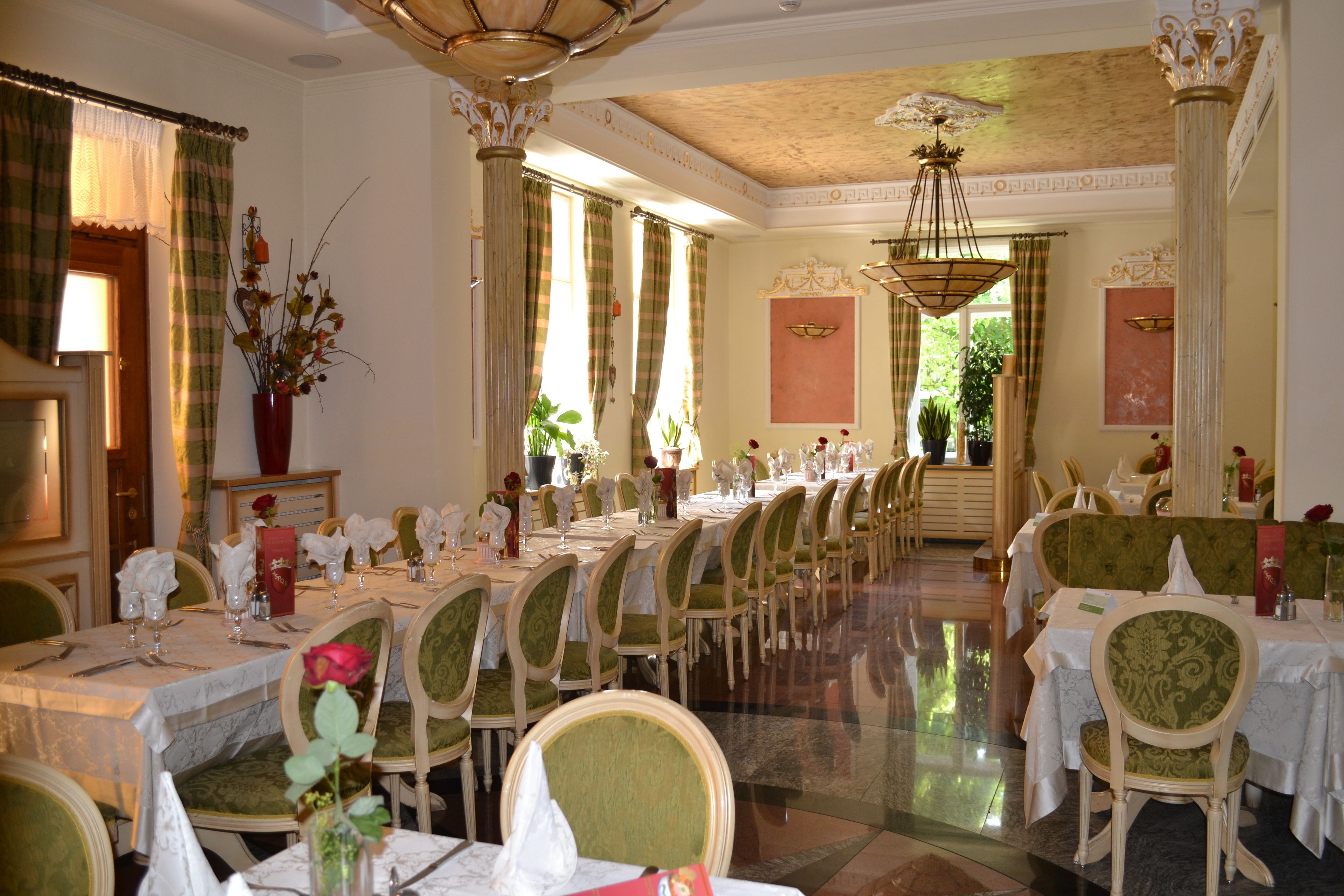 A formal dining room with multiple tables set for service, chairs with green upholstery, and a chandelier.