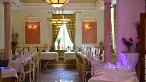 Un comedor formal con varias mesas dispuestas para una comida, candelabros elegantes y apliques decorativos en las paredes.