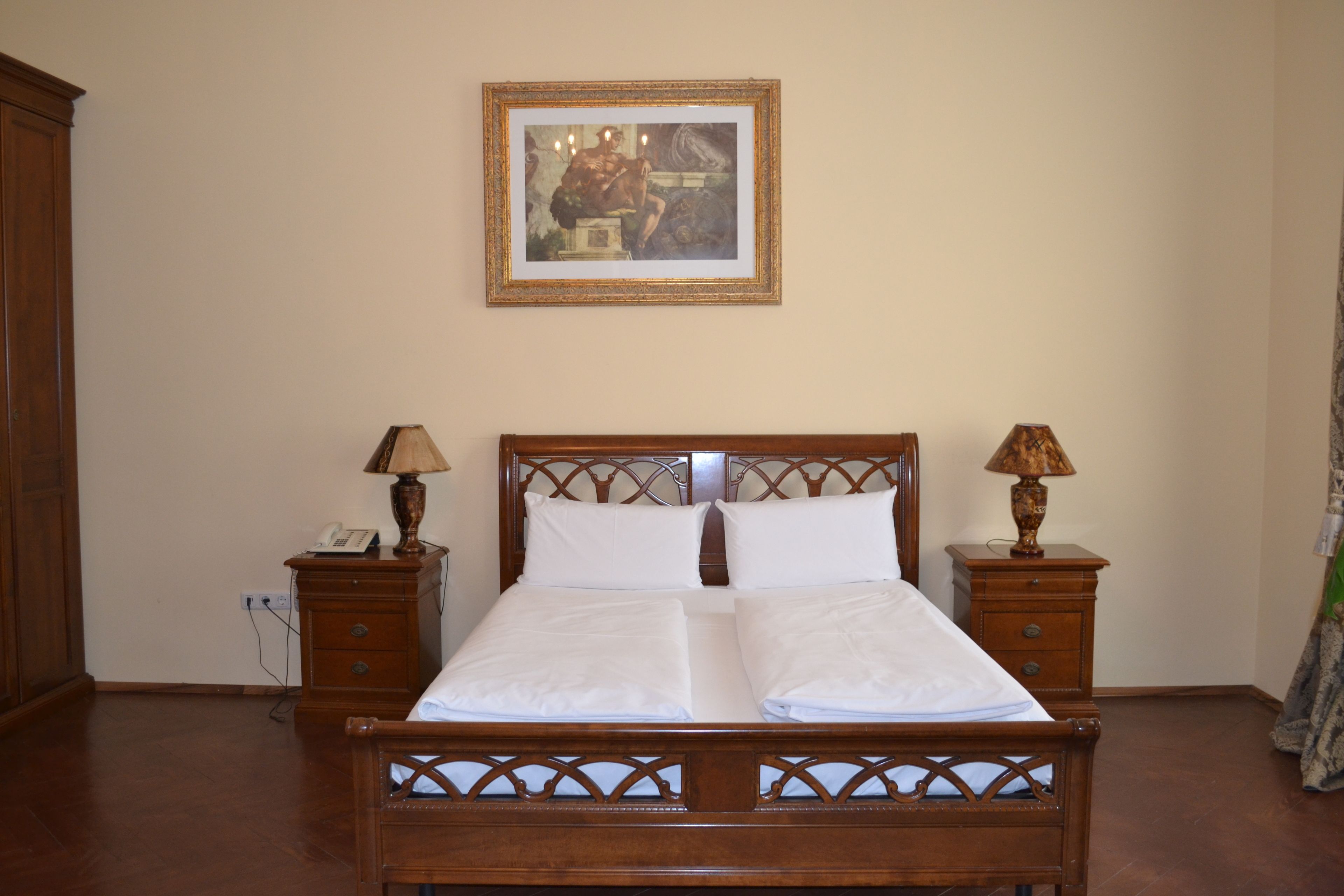 A neatly made bed with white linens, two bedside tables with lamps, a wooden headboard, and a framed picture on the wall.