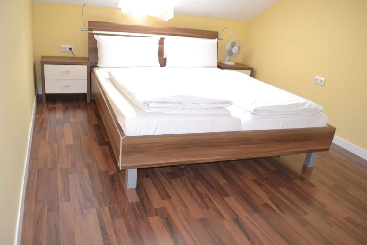 A neatly made bed in a room with wooden flooring, a bedside table, and a nightstand.