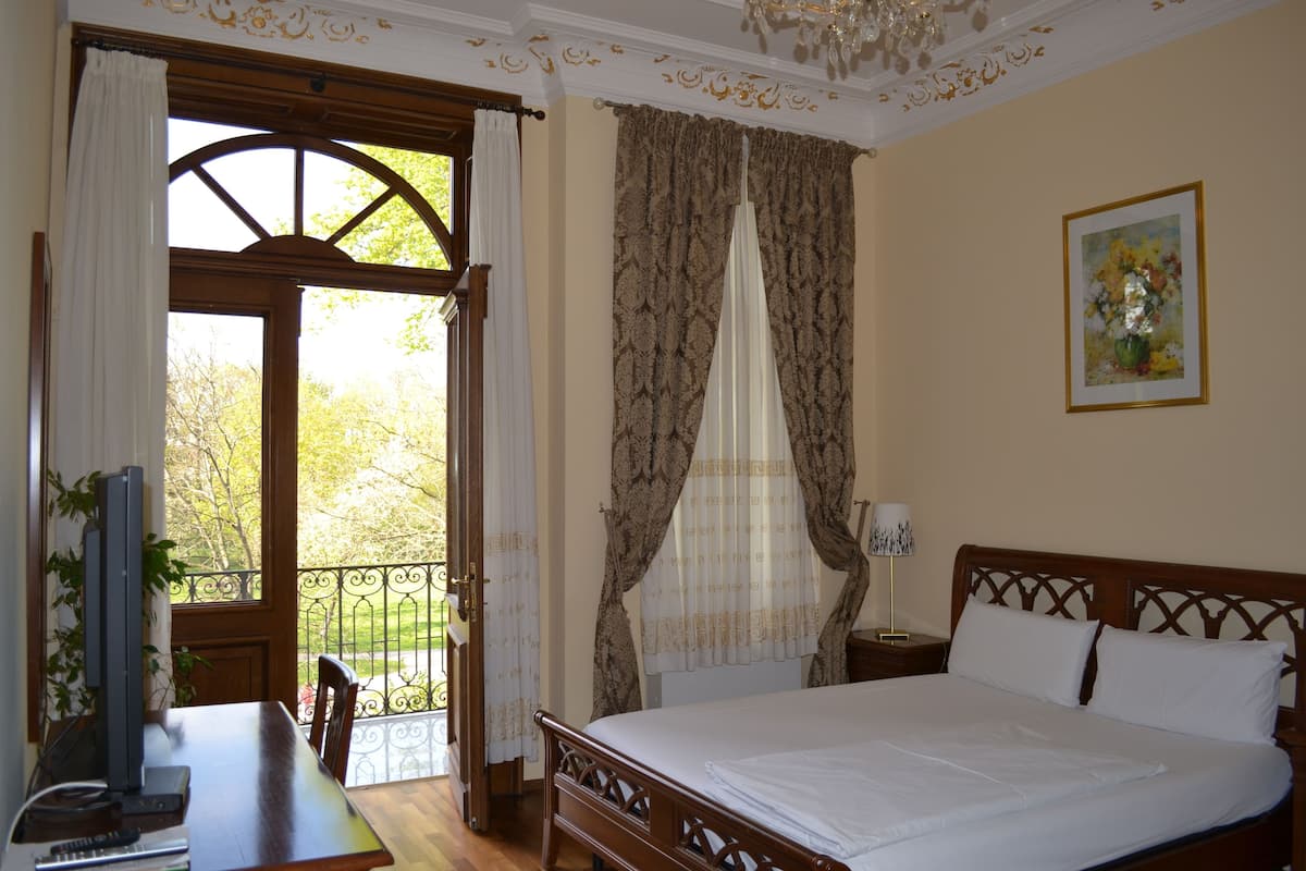 A bedroom with a wooden bed, a desk with a computer, and a window with curtains.