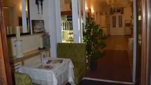 Un vestíbulo de hotel con un sillón verde, una mesa con una revista, una planta en maceta y un espejo que refleja la habitación.