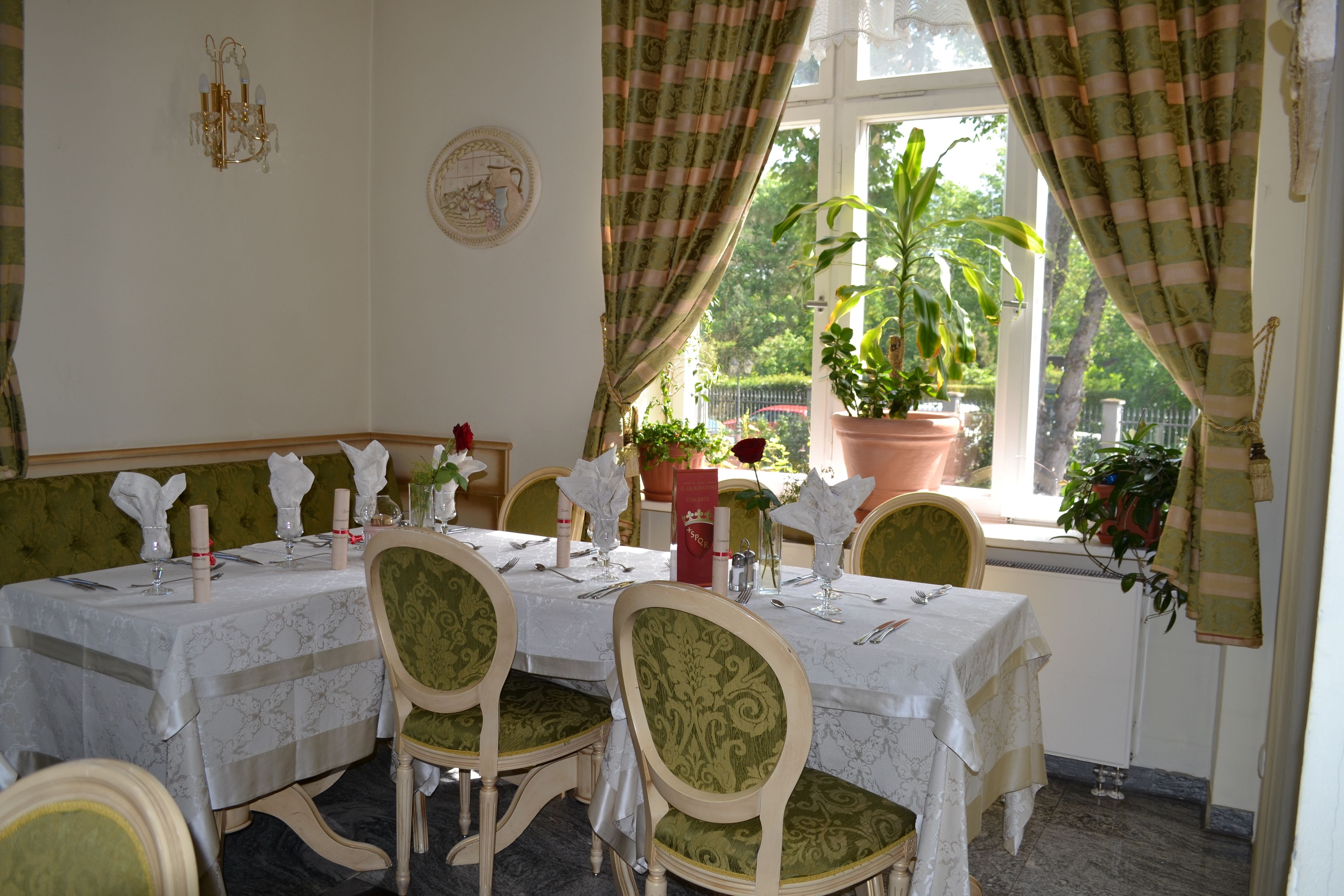 A dining area with a table set for six, green upholstered chairs, and a large window with curtains.
