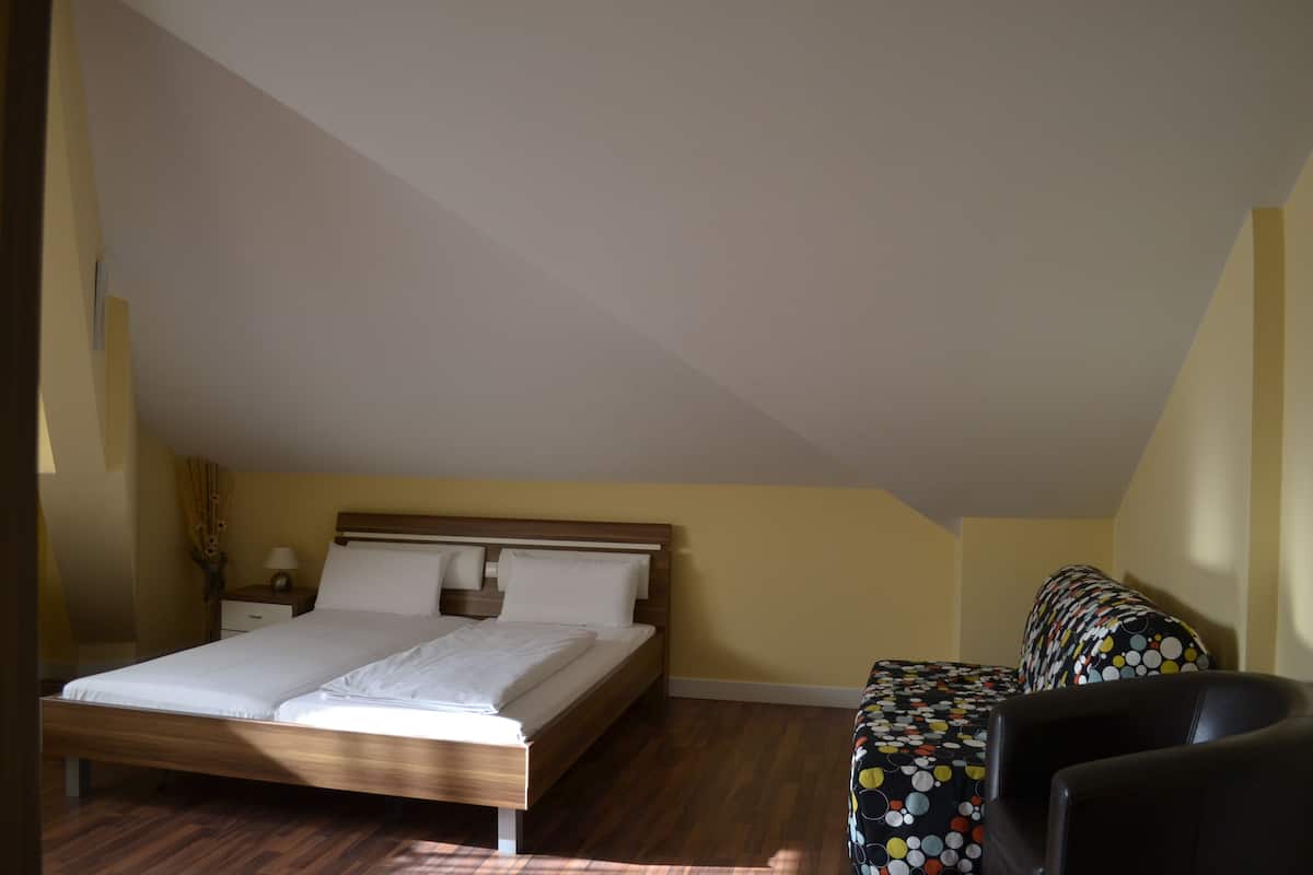 A bedroom with a wooden bed, a nightstand, a chair, and a patterned sofa.
