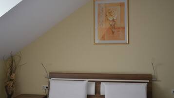 A bedroom with a wooden headboard, two white pillows, a framed artwork of a rose, and a nightstand with a vase of dried plants.