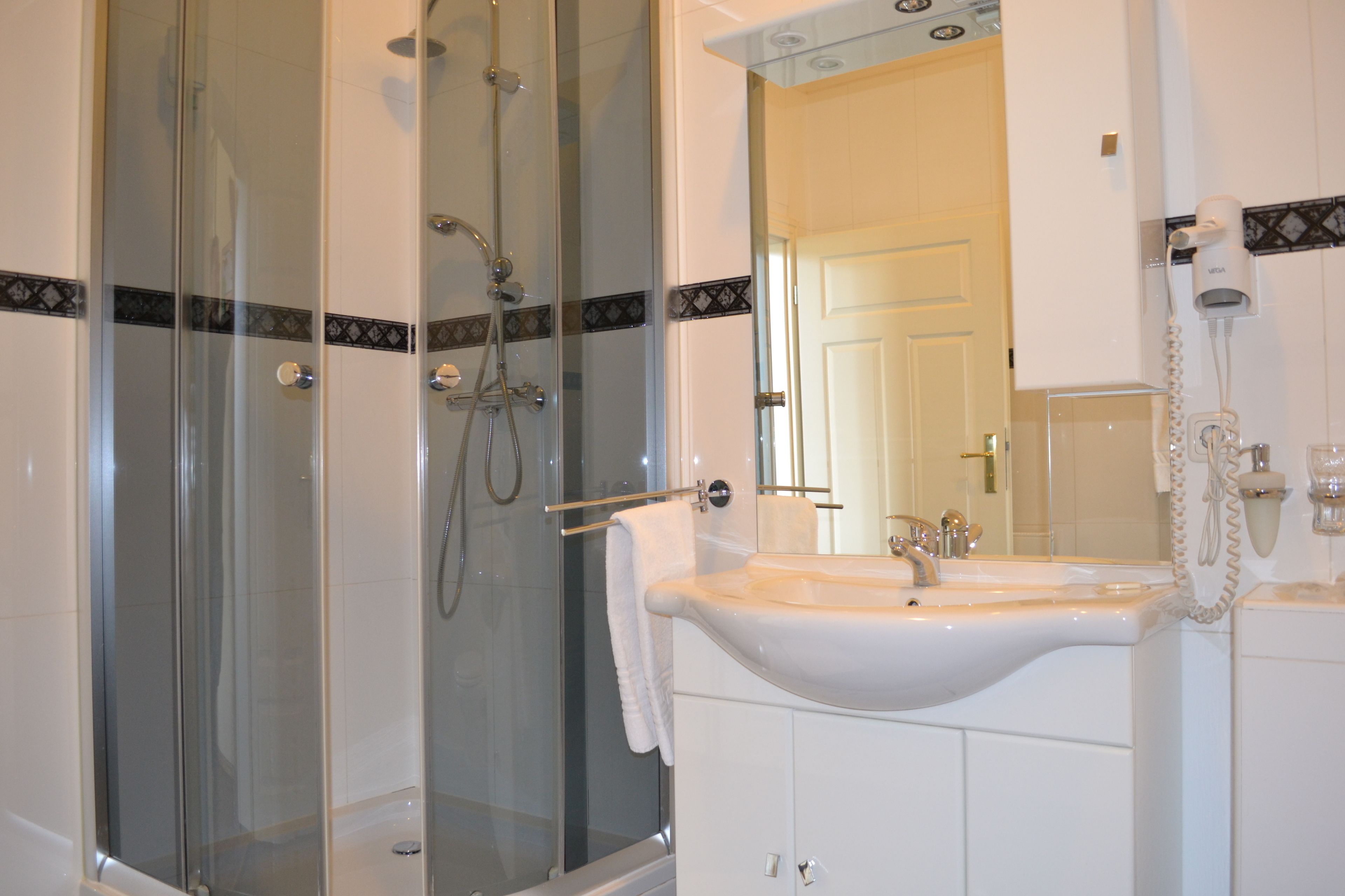 Un baño moderno con ducha de vidrio, lavabo blanco y un espejo grande.