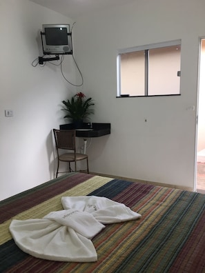 A room with a bed, a desk, a chair, a television mounted on the wall, and a window. - Pousada Vintage (Assis)