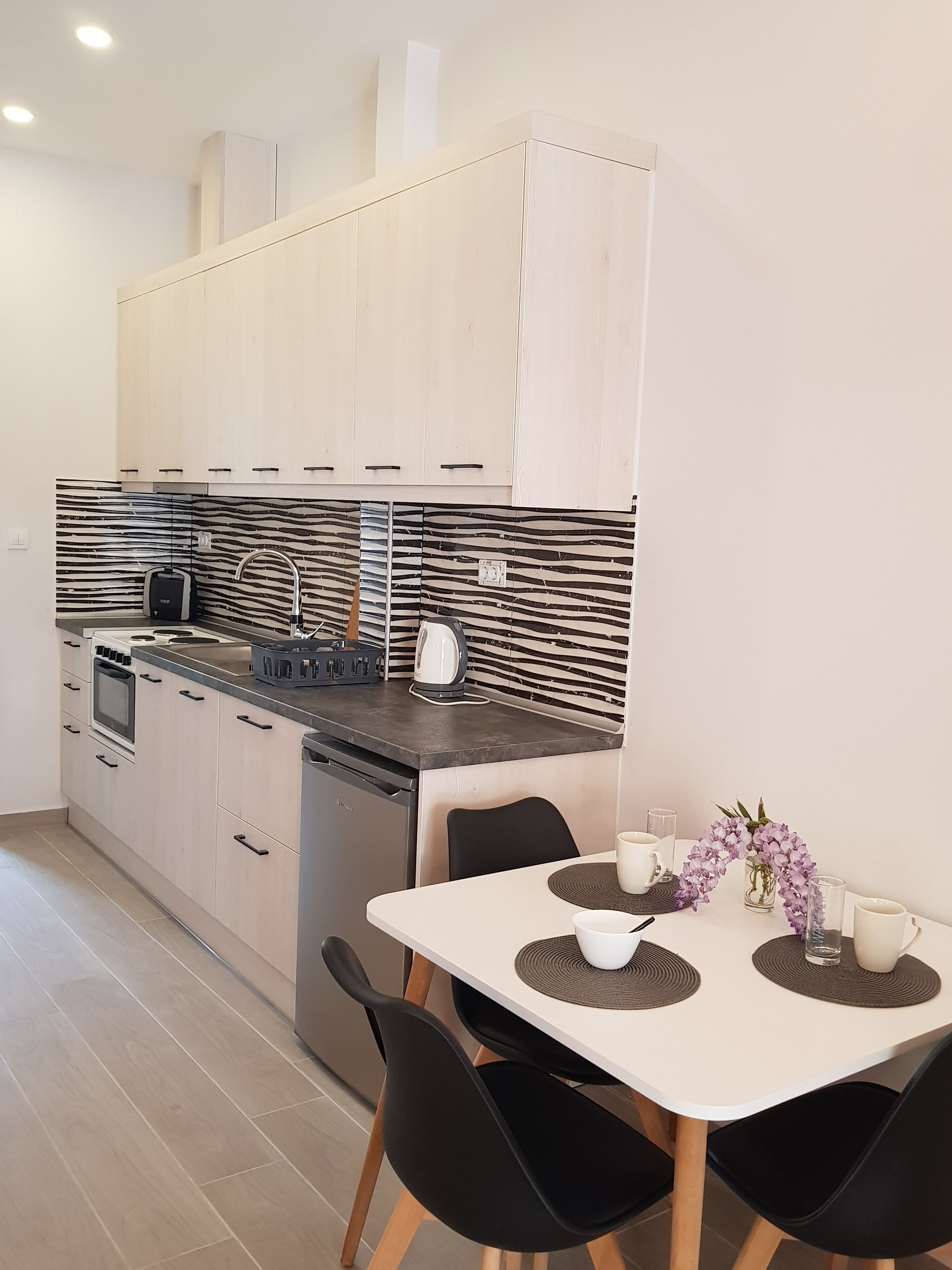 A modern kitchen with light wood cabinets, a black and white backsplash, and a dining area with a white table and black chairs.
