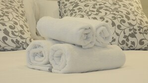 A neatly made bed with white linens and rolled towels, set against a backdrop of patterned pillows. - Old City House (San Sebastián)