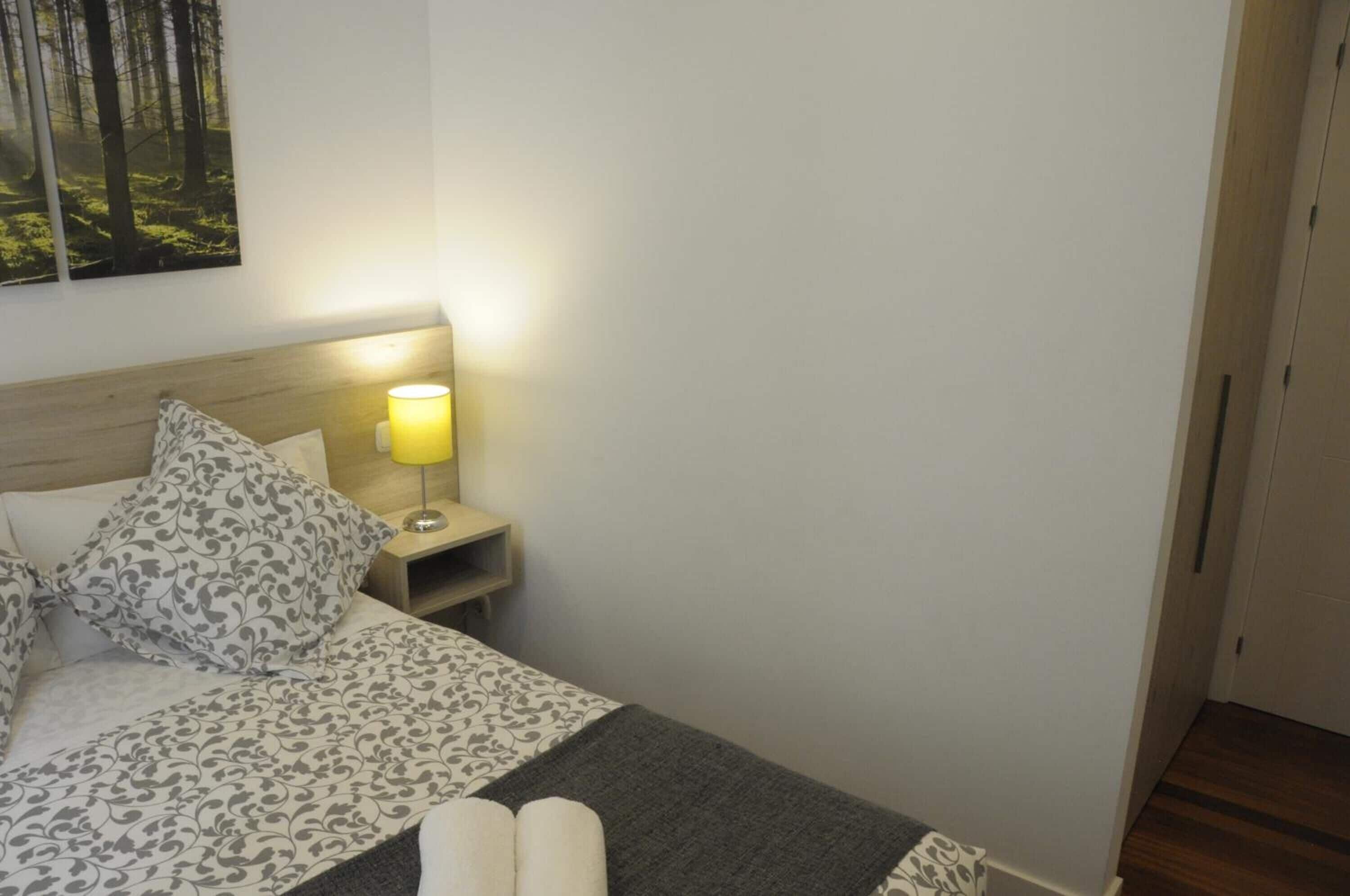 Een net opgemaakt bed met beddengoed met een patroon, een bedlamp en een ingelijst foto aan de muur.